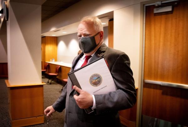 Gov. Tim Walz wearing a COVID mask and clutching a binder under his left arm.