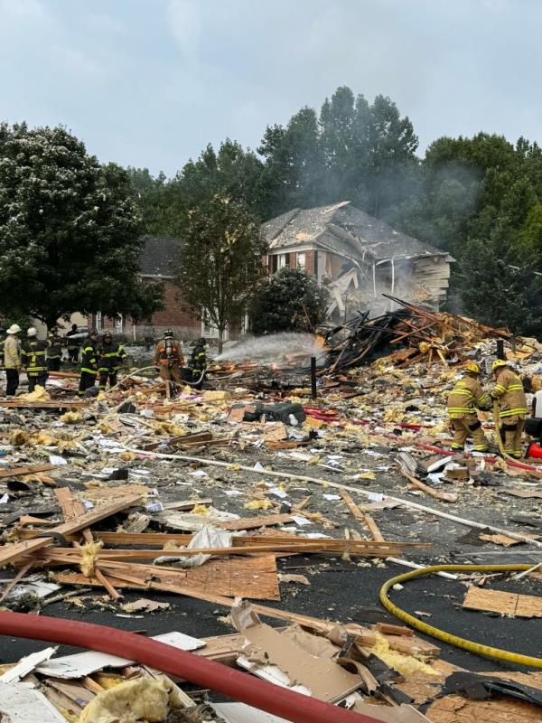 Firefighters work to put out the smoldering remains of the house,  with debris scattered across the street.