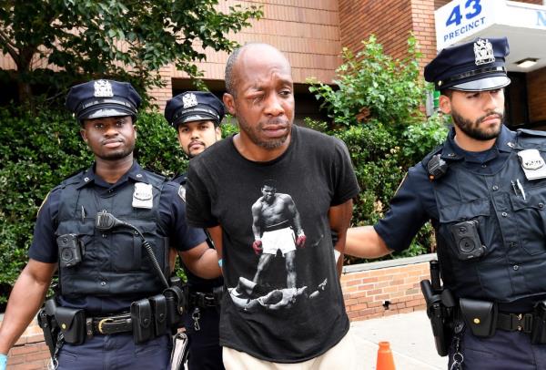 Cops hold the handcuffed arms of Ernst Delma, who's wearing a Muhammad Ali t-shirt.