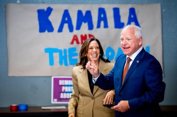 Democratic presidential nominee Kamala Harris and her running mate, Minnesota Gov. Tim Walz smiling in front of a large hand painted sign which reads kamala and the coach