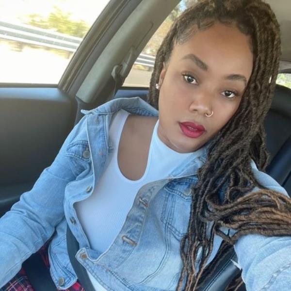 A woman in a car taking a selfie, identified as Autumn Clark, involved in a cryptocurrency theft case. Seen in white shirt and denim jacket, with nose ring and braids, in car selfie.