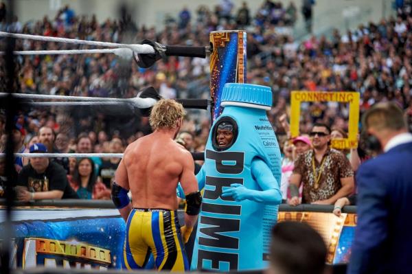 The back of Logan Paul and KSI in a Ormu drink costume in the ring during WrestleMania with a crowd watching in the background.